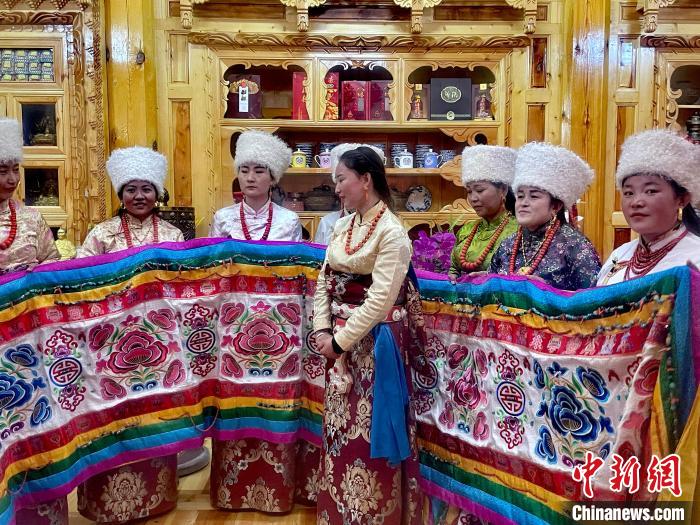 圖為女性展示村民自發(fā)繡制的“百米五彩哈達(dá)”?！±钣穹?攝